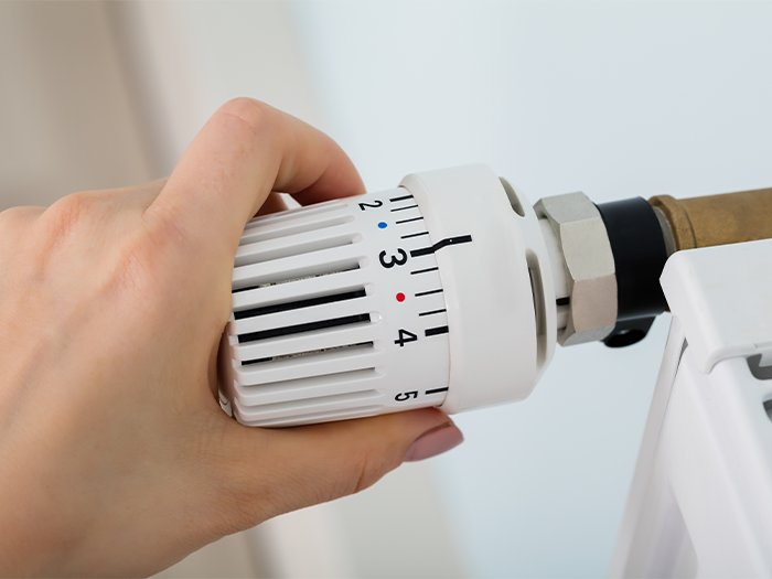 Hand stellt ein Heizkörperthermostat auf Stufe drei ein.